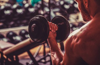 Bodybuilder working out with dumbbell weights at the gym. Man bodybuilder doing exercises with dumbbells. Fitness man lifting dumbbell.