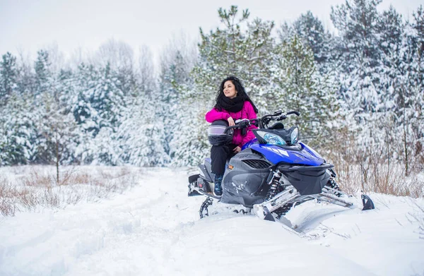 Woman is riding snowmobile in mountains. Girl on a sports snowmobile in a mountain forest. Athlete rides a snowmobile in the mountains. Snowmobile in snow. Concept winter sports.