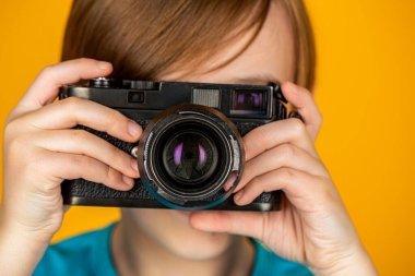 Stüdyodaki çocuk profesyonel kamerayla. Kamera kullanan bir çocuk. Kameralı bebek. Elinde kamerayla gülümseyen neşeli bir çocuk. Küçük bir çocuk eski model bir kamera kullanarak fotoğraf çekiyor..