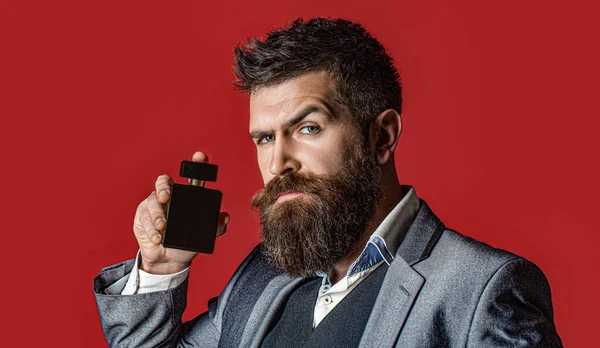 Male holding up bottle of perfume. Man perfume, fragrance. Perfume or cologne bottle, perfumery, cosmetics, scent cologne bottle, male holding cologne. Masculine perfumery, bearded man in a suit.