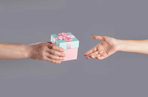 Male and female hands holding pink gifts box. Girl gives a gift to man. Woman hands holding gift. Gift box in hand, surprise and holiday concept. Man hands holding valentines day gift.