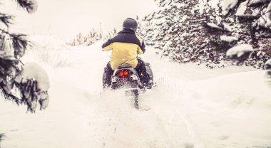 Sporcu dağlarda kar motosikletine biner. Karda kar arabası. Kış sporları kavramı. Adam dağlarda kar motosikleti sürüyor. Dağ ormanlarında kar motosikletli bir pilot..