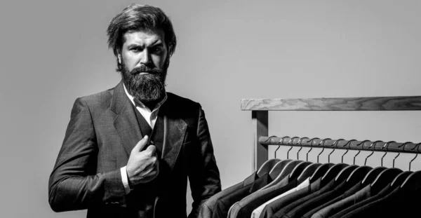 Tailor, tailoring. Mens suit, tailor in his workshop. Elegant mans suits hanging in a row. Luxury mens classic suits on rack in elegant mens boutique.