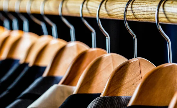 Mens suits in different colors hanging on hanger in a retail clothes store, close-up. Mens shirts, suit hanging on rack. Hangers with jackets on them in boutique. Suits for men hanging on the rack.