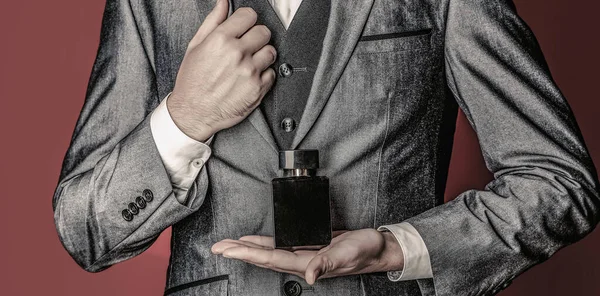 Men perfume in the hand on suit background. Man in formal suit, bottle of perfume, closeup.