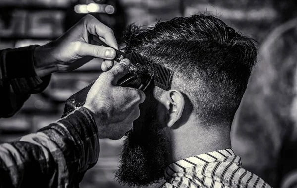 Haircut concept. Man visiting hairstylist in barbershop. Barber works with hair clipper. Hipster client getting haircut. Black and white.