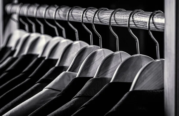 Mens shirts, suit hanging on rack. Hangers with jackets on them in boutique. Suits for men hanging on the rack. Black and white.