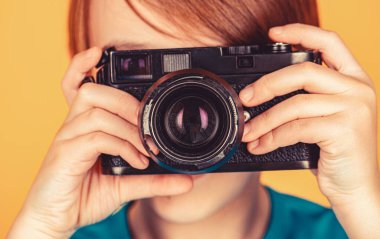 Elinde kamerayla gülümseyen neşeli bir çocuk. Eski model bir kamera kullanarak fotoğraf çeken küçük bir çocuk. Stüdyodaki çocuk profesyonel kamerayla. Kamera kullanan bir çocuk. Kameralı bebek..