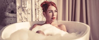 Saflık ve rahatlık kavramı. Güzel kızıl saçlı kız köpük banyosu yapıyor. Banyodaki güzel kadın..