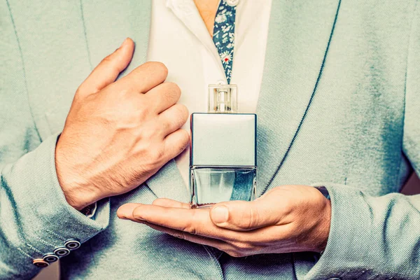 Masculine perfume, bearded man in a suit. Male holding up bottle of perfume. Perfume or cologne bottle and perfumery, cosmetics, scent cologne bottle.