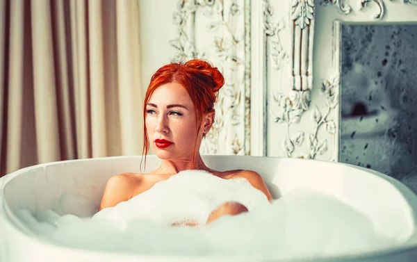 漂亮的红头发少女在泡泡浴 浴室里漂亮的女人洗澡 快乐的年轻女人红头发躺在浴缸里放松 — 图库照片