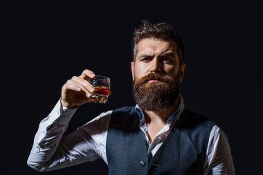 Sakallı adam cam brendi tutuyor. Sakallı konyak. Sommelier içkinin tadını alır. Elinde bir bardak viski tutan bir adam. Viski yudumluyor. Kalın sakallı bir adamın portresi. Maço içki. Degukasyon, tatma.