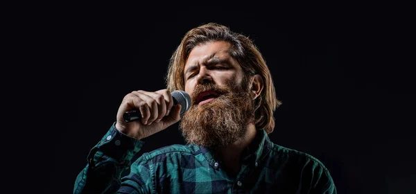 Bearded man singing with microphone. Male singing with a microphones. Man with a beard holding a microphone and singing. Bearded man in karaoke sings a song into a microphone. Male attends karaoke.