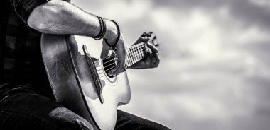 Gitar akustiği. Gitar çalan erkek müzisyen, müzik aleti. Akustik gitar çalan erkek elleri, yakın çekim. Siyah ve beyaz.
