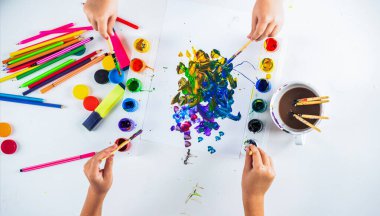 Çocuk resim malzemeleriyle masayı boyuyor. Suluboya lekeli fırça boyalı eller. Beyaz bir kağıt üzerine çizim yapmak. Yaratıcılık ve sanat. Eller boya fırçası.