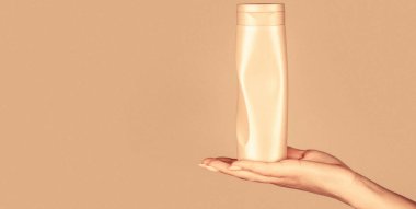 Vücut losyonlu konteynır. Kozmetik şişeli kadın elleri. Ellerinde saç kremi şişesi var. Şampuan şişesi elinde. Saç bakımı için jel dağıtıcı.