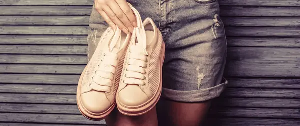 Woman holding shoes. Woman holding a pair of pink shoes. Girl with a beautiful waist in jeans shorts.