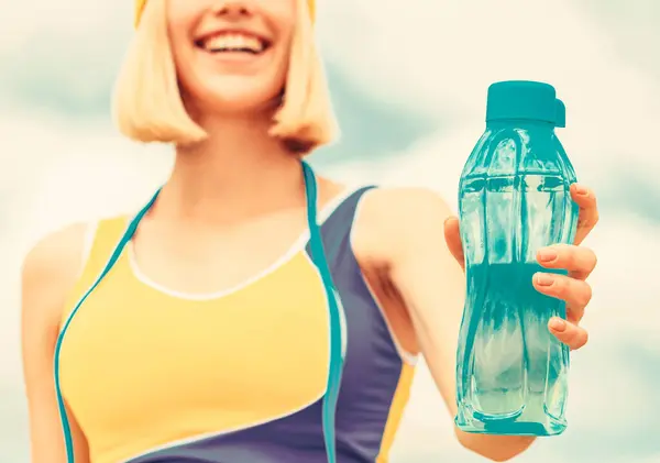 Woman drinking water after run. Sports girl drinks water from a bottle on a sky background. Drinking during sport.