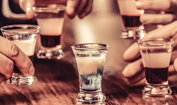 Friends drink shot or liqueur. Group friends tequila shot glasses in bar. Male hands glasses of shot or liqueur.