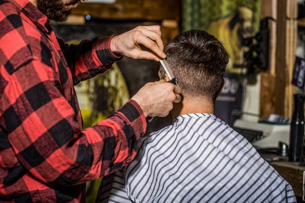 Haircut concept. Man visiting hairstylist in barbershop. Barber works with hair clipper. Hipster client getting haircut. Hands of barber with hair clipper, close up.