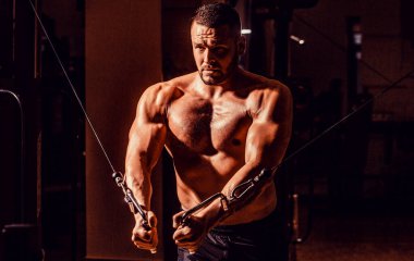 Spor salonunda egzersiz makinesi kablolu yayını. Spor salonunda kaslı yakışıklı bir adam. Spor salonundaki makine. Abs ve biceps..