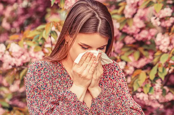 Pollen allergy, girl sneezing. Allergy, sneezing, spring. Woman sneezing in front of blooming tree. Spring allergy concept.