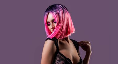 Saçları ultra pembeye boyanmış güzel bir kız. Güzellik salonunda yapılan şık bir saç stili. Kızıl saçlı. Pembe kıvırcık, sağlıklı, parlak saçlar ve gri arka planda makyaj..
