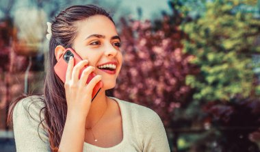 Neşeli bir kadın telefonda konuşuyor. Gülümseyen kız dışarıda cep telefonuyla konuşuyor. Açık havada akıllı telefon kullanan çekici bir kadın, bahar havası..
