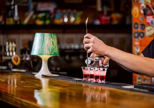 Red alcoholic drink in glasses on bar. Red cocktail at the nightclub. Barman preparing cocktail shooter. Bartender pouring strong alcoholic drink into small glasses on bar. Shots at the nightclub.