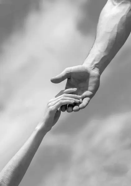 Rescue, helping gesture or hands. Solidarity, compassion, and charity, rescue. Hands of man and woman on sky background. Lending a helping hand. Black and white.