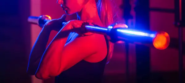 Woman lifting barbells, working out in a gym. Fit girl doing squats with barbell in gym. Girl muscular body exercising. Sports woman with barbell.