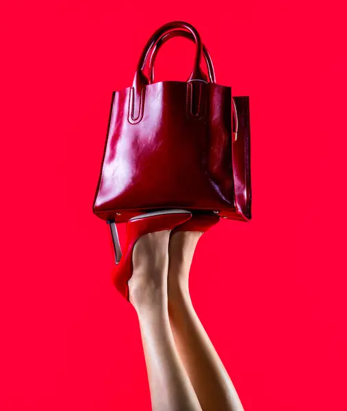 Stylish red female leather bag. Perfect female legs wearing high heels. Shapely legs, a girl in shoes high-heeled. Red glossy female leather bag.