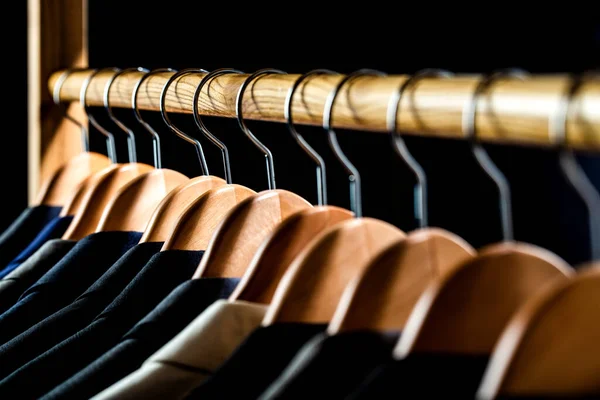 Mens shirts, suit hanging on rack. Hangers with jackets on them in boutique. Suits for men hanging on the rack. Mens suits in different colors hanging on hanger in a retail clothes store.