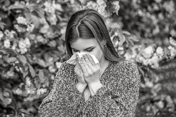 Pollen allergy, girl sneezing. Allergy, sneezing, spring. Woman sneezing in front of blooming tree. Black and white.