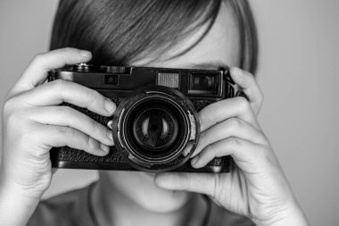 Kameralı çocuk. Elinde kamerayla gülümseyen neşeli bir çocuk. Eski model bir kamera kullanarak fotoğraf çeken küçük bir çocuk. Siyah ve beyaz.
