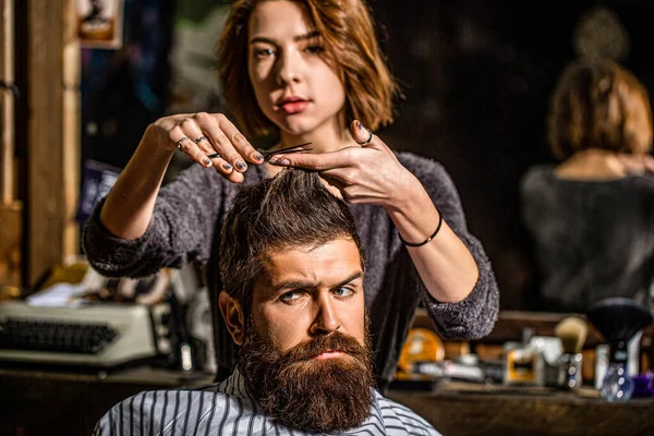 Working hair scissors. Professional barber girl cutting hair of bearded man. He is getting haircut at barbershop. Barbershop, beauty salon. Beard man in barbershop. Barber scissors, barber shop.