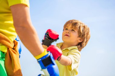 Baba oğlunu boks eğitiyor. Büyükbaba çocuk boks pozisyonunda duruyor. Dövüşçü. Kırmızı boks eldivenli küçük çocuğa koçluk yapan bir adam. Küçük çocuk boks yapıyor büyükbaba..