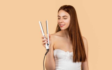 Saç stili. Güzel, gülümseyen bir kadın. Uzun saçları düz ütülüyor. Saçı düzleştirici ile düzelten mutlu kadın. Parlak saçlarında stilisti olan güzel bir kızın portresi..