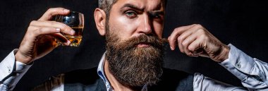 Sakallı adam elinde brendi bardağı tutuyor. Tatma ve degukasyon konsepti. Zarif takım elbiseli sakallı bir işadamı ve bir bardak viski. Viski, konyak, konyak içen bir adam. Degukasyon, tatma.