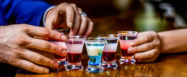 Man hands glasses of shot or liqueur. Glasses of alcohol. Tequila shots, vodka, whisky, rum. Group friends tequila shot glasses in bar.