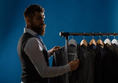 Terzi, terzilik. Erkek kıyafeti, atölyesinde terzi. Zarif adamlar peş peşe asılıyor. Lüks erkekler şık erkek mağazasında raflarda klasik takım elbiseler..