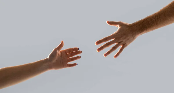 Hands man and woman reaching to each other, support. Giving a helping hand. Hands of man and woman on gray background. Lending a helping hand. Solidarity, compassion, and charity, rescue.