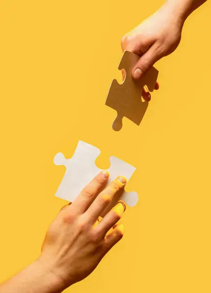 Closeup hands of man connecting jigsaw puzzle. Two hands trying to connect couple puzzle with yellow background. Hand connecting jigsaw puzzle. Man hands connecting couple puzzle piece.