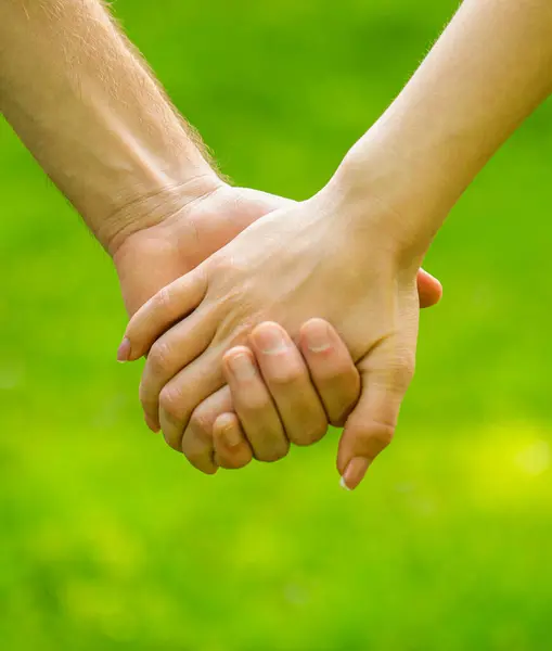 Couple hold hand in the autumn or summer park. Closeup of loving couples holding hands while walking. Female and male hand together. Couple holding hands in the park.
