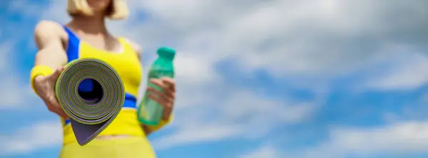 Woman in sports wear is holding a yoga mat and a bottle of water. Yoga mat and water bottle. Healthy lifestyle concept.