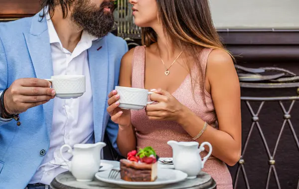 Smiling young woman kissing boyfriend while having coffee at cafe. Couple drinking coffee in restaurant. They drinking tea at cafe in street. Holding cup. Enjoying their date. Hugging, kiss.