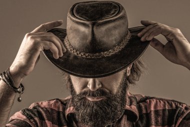 Kovboy tarzı. Kovboy şapkasını ayarlayan yakışıklı genç adam. Şapkalı kovboylar. Yakışıklı sakallı maço. Tıraşsız kovboylar. Amerikan kovboyu. Deri kovboy şapkası..