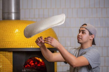 Skilled chef preparing dough for pizza rolling with hands and throwing up. The chef tosses the pizza dough into the air. Hands of a male chef with thin round pizza dough in the kitchen. clipart