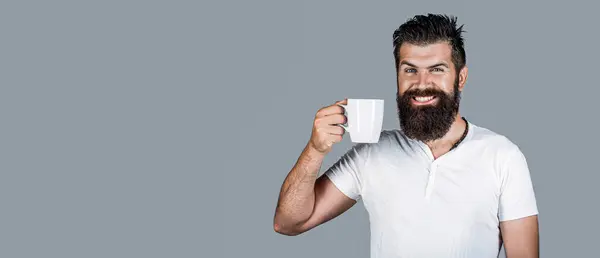 Smiling bearded hipster man holding cup of coffee or tea. Handsome mans holds cup of coffee, tea. Bearded man smiling. Good morning, man tea. Smiling hipster man with cup of fresh coffee, happy man.