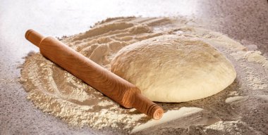 Taze çiğ hamur ve rulo. Pizza ya da ekmek pişirmek için çiğ hamur. Yuvarlak hamur hamuru ve masa üzerinde merdane ile pişirilmiş un. Yeni hazırlanmış hamur ve un karıştırıcı ile ahşap bir oklava..